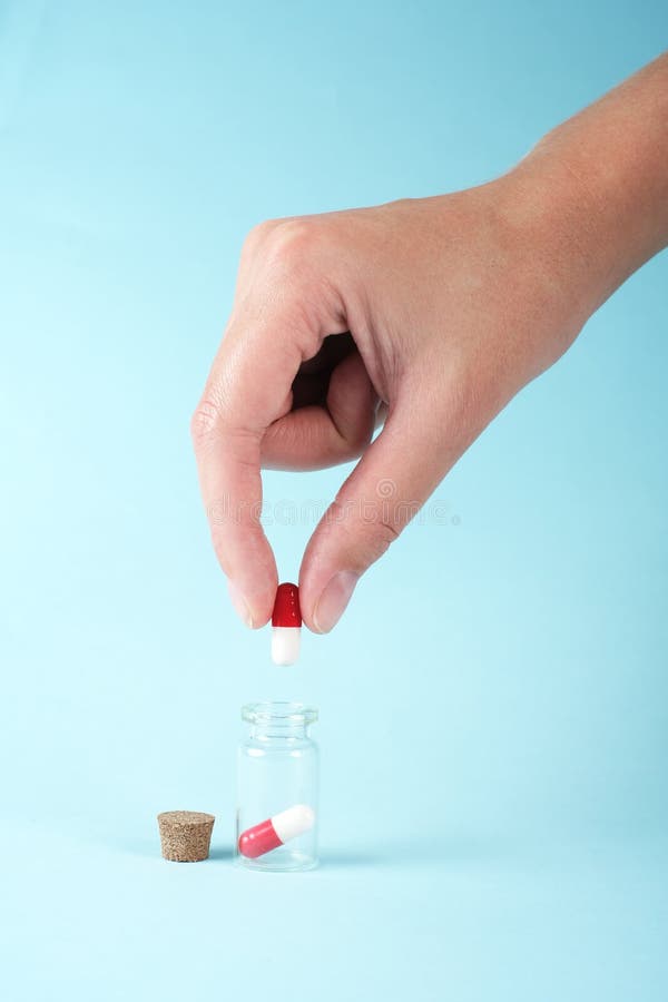 Man`s hand holds a pill over a transparent jar with medicines on a light background close-up. vitamins. pharmaceuticals. chemical industry. remedies for viruses and bacteria. red and white pills