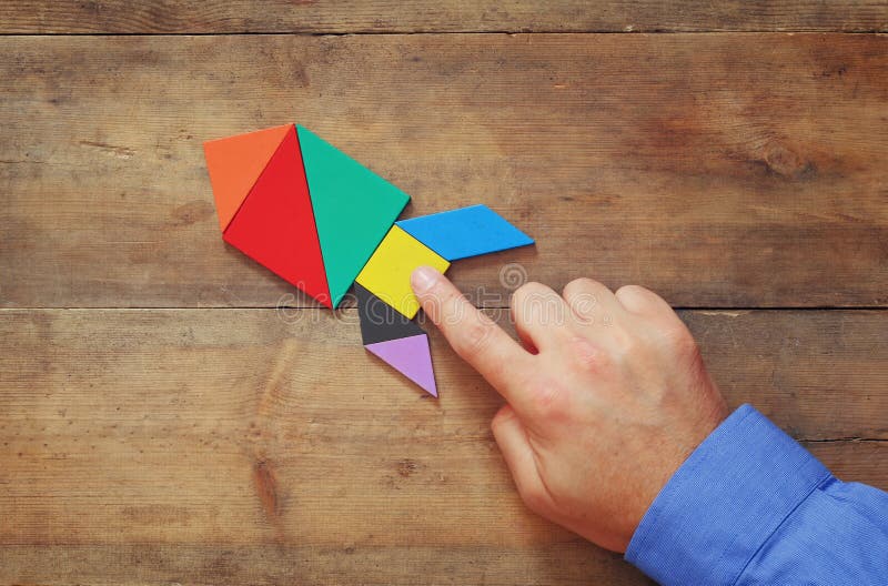 Man's hand pointing at rocket made from square tangram puzzle stock photo