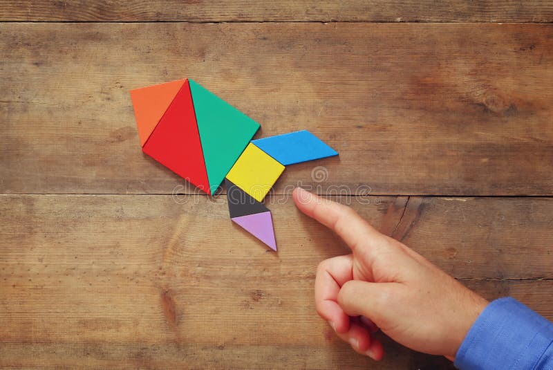 Man's hand pointing at rocket made from square tangram puzzle royalty free stock photography