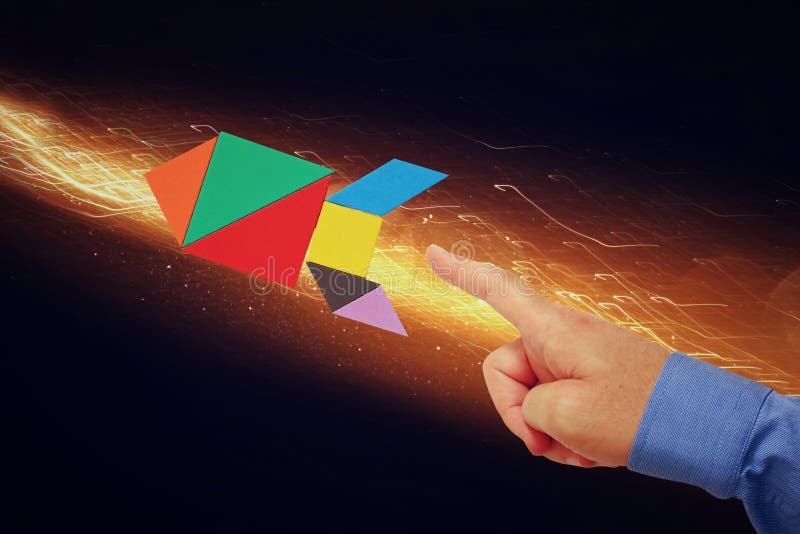 Man's hand pointing at rocket made from tangram puzzle stock image