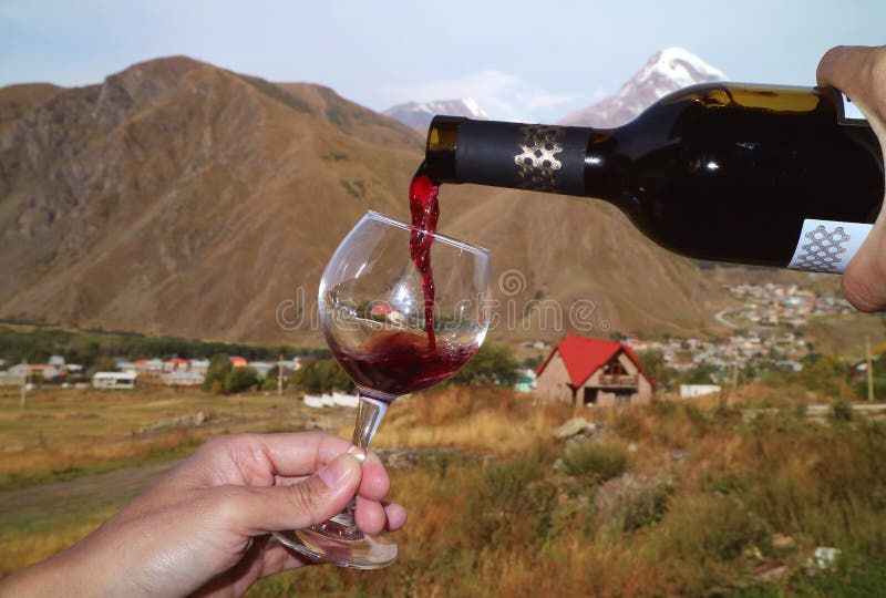 Man`s hand pouring red wine from the bottle into wineglass at the village of Mount Kazbek