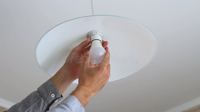 A man`s hand is screwing an light bulb into a chandelier in the kitchen