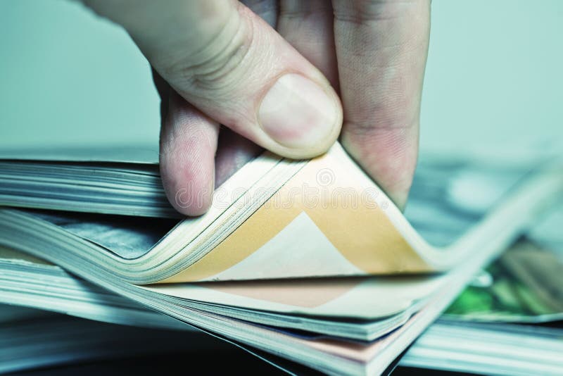 Man s hand turned over a stack of magazines