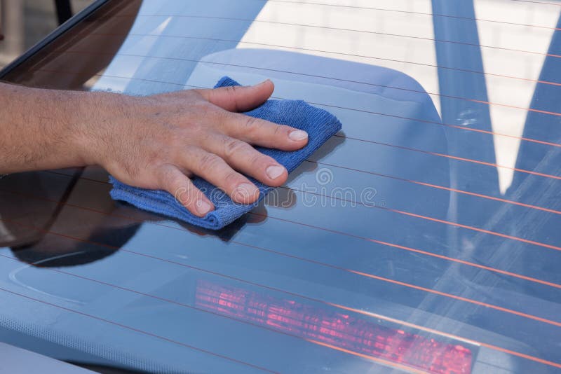 Man`s hand washes and cleans the car window with a rag.