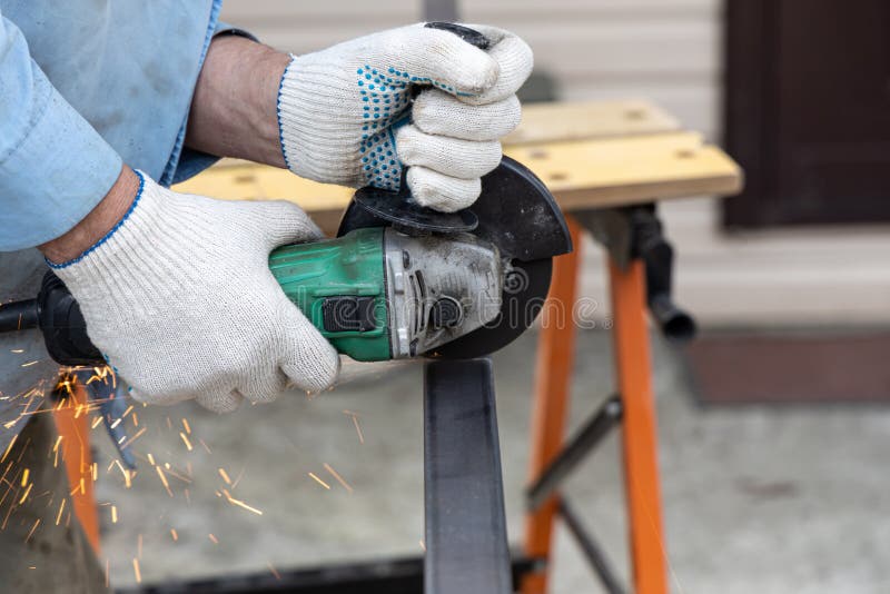A Man in the Safety Gloves is Cutting Metal Using a Green Angle Grinder