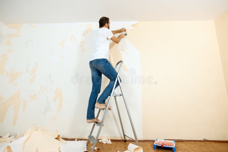 Man in with a Scraper in the Process of Removing Old Wallpaper. Stock