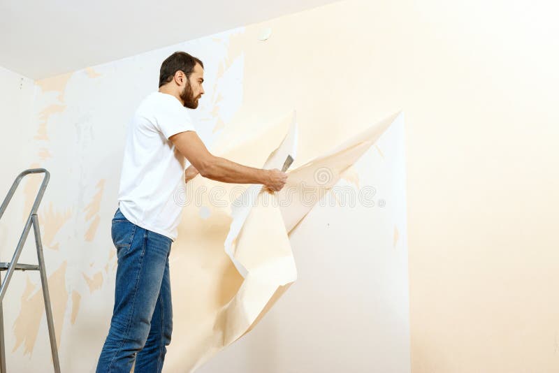 Man in with a Scraper in the Process of Removing Old Wallpaper. Stock