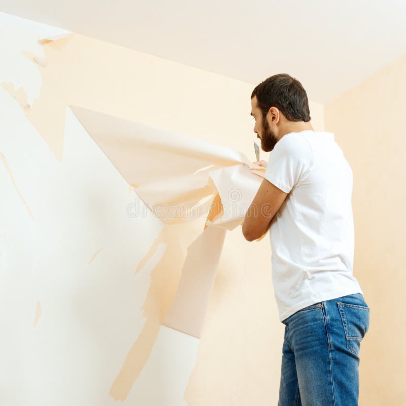 Man in with a Scraper in the Process of Removing Old Wallpaper. Stock