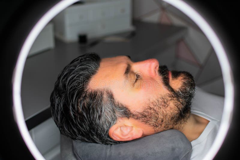 Man seen through ring light while relaxing at beauty salon. Image showing man relaxing during a male grooming beauty treatment. Photo taken through a bright ring stock photos Man seen through ring light while relaxing at beauty salon. Image showing man relaxing during a male grooming beauty treatment. Photo taken through a bright ring stock photos