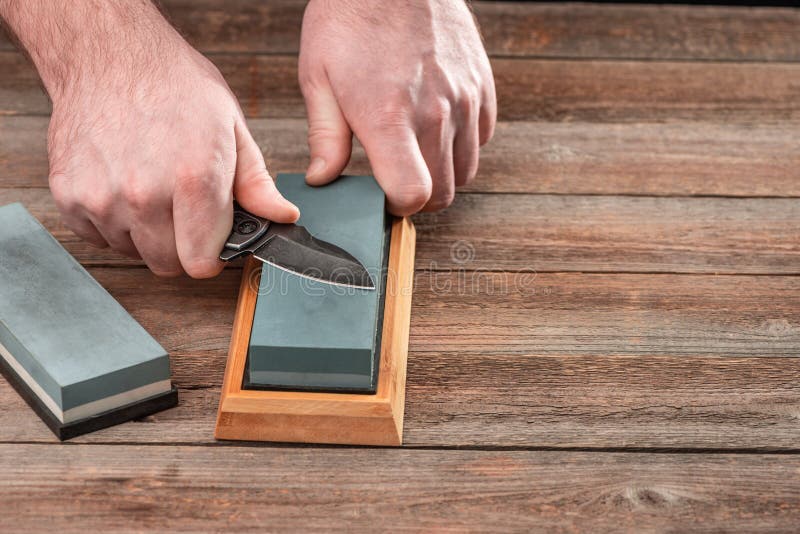 Man Sharpening His Pocket Knife with a Whetstone on a Rustic