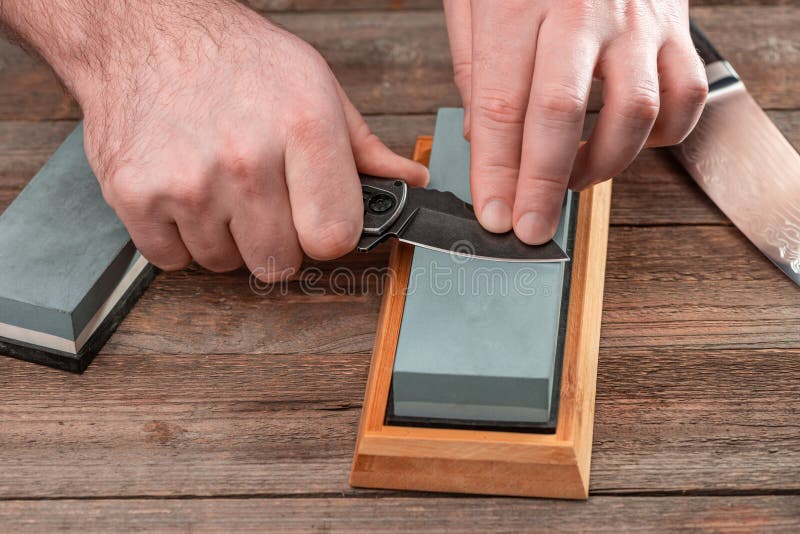 Man Sharpening His Pocket Knife with a Whetstone on a Rustic