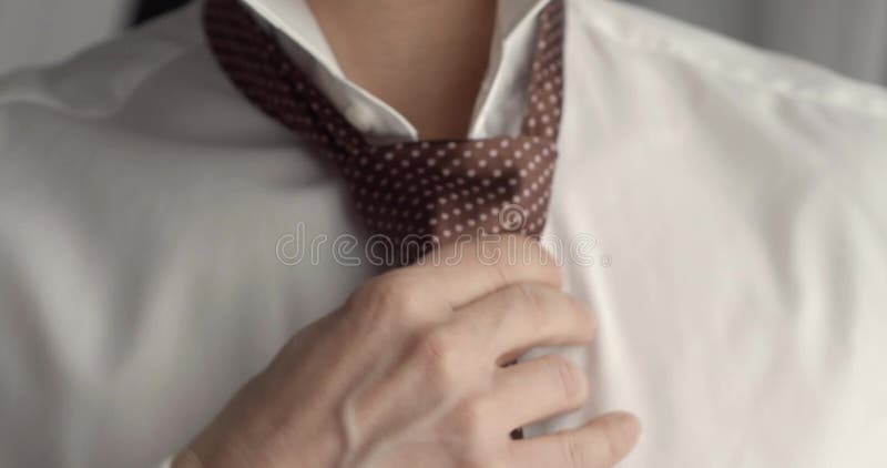 Man in shirt dressing up and adjusting tie on neck at home