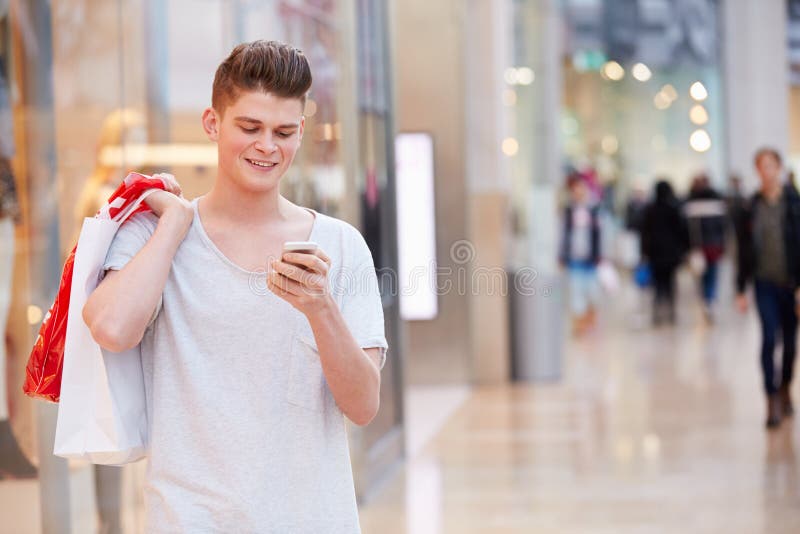 Man In Shopping Mall Using Mobile Phone To Text Whilst Holding Shopping Bags