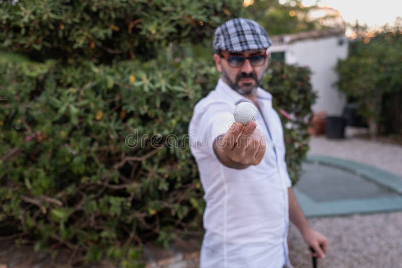 Man Showing Golf Ball in His Hands with Golf Club on His Back Stock