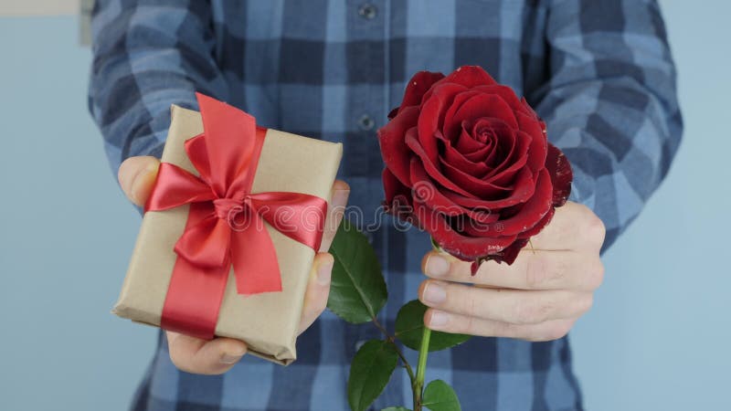 Man is showing present gift box and red rose towards to camera. Hands hold presents for St. Valentine`s Day or International Women