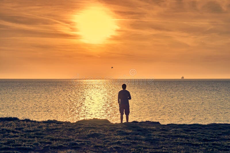 Man silhouette standing on a beach and watching a sunrise