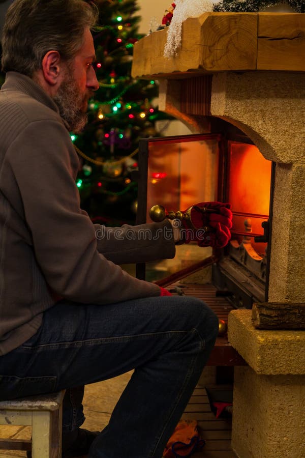 Man sits in front of burning fireplace. Behind Christmas tree royalty free stock photography