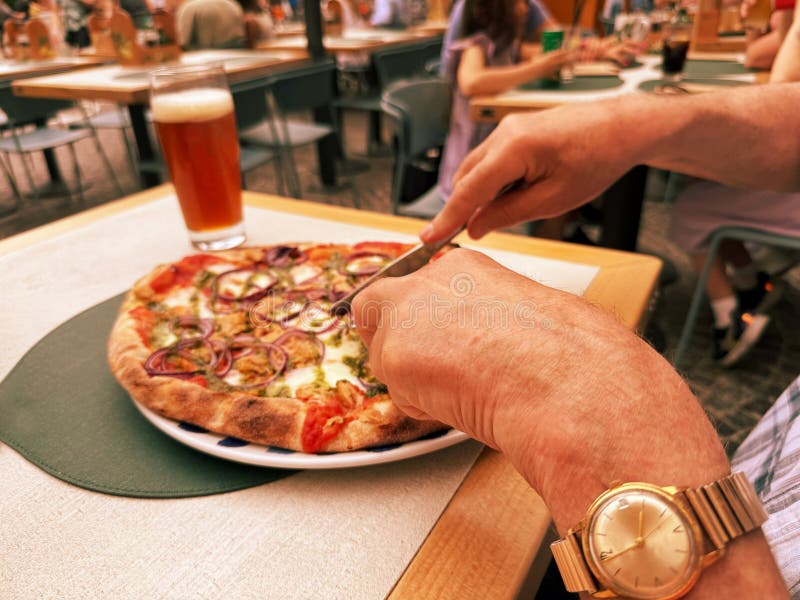 A man sits at a table in a restaurant and eats pizza with a knife and fork. He drinks a beer with it. Selective focus royalty free stock photos
