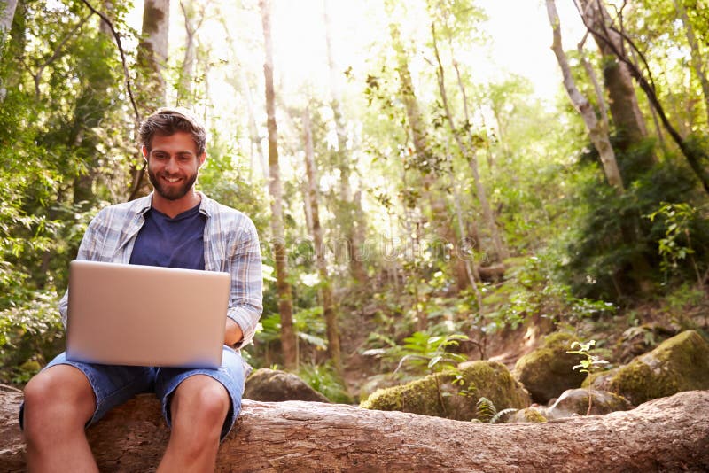 Man Sits On Tree Trunk In Forest Using Laptop Computer stock images Man Sits On Tree Trunk In Forest Using Laptop Computer stock images