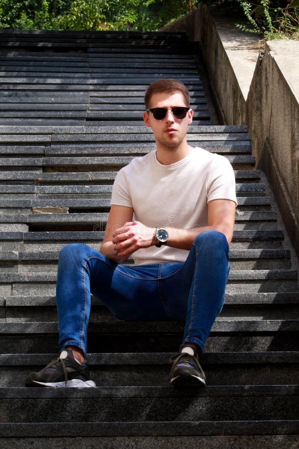 Man sitting alone on steps. Handsome boy with sunglasses. Male model posing for shooting, sitting on old stairs.