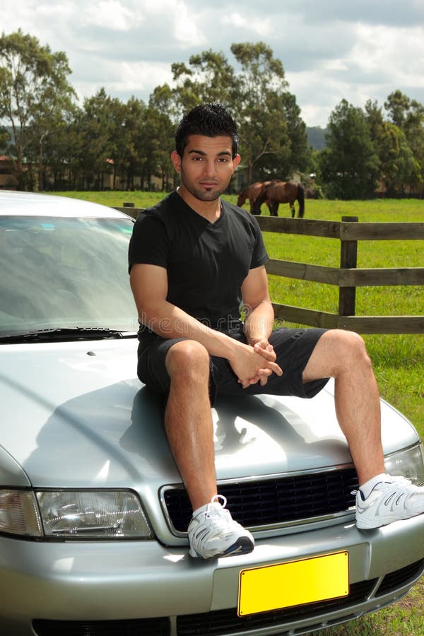 Man sitting on bonnet of silver car in countryside. 