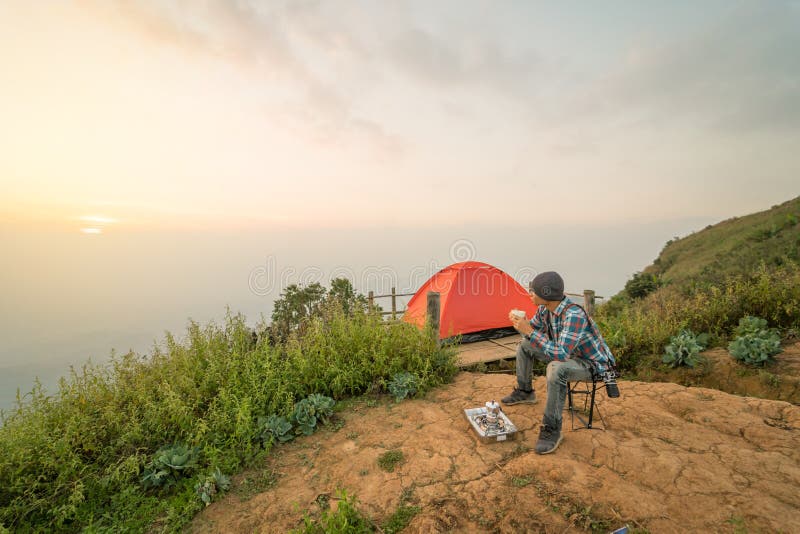 Man sitting and drinking coffee near camping tent