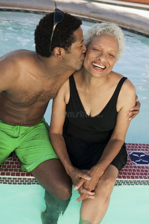 Man sitting on edge of swimming pool kissing mother on cheek elevated view.