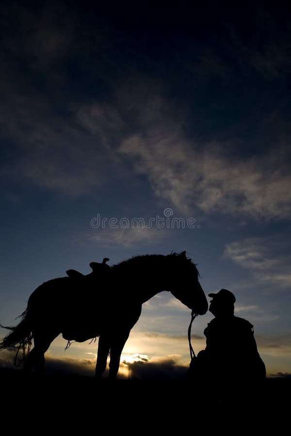 A cowboy sitting on the ground beside his horse. A cowboy sitting on the ground beside his horse.