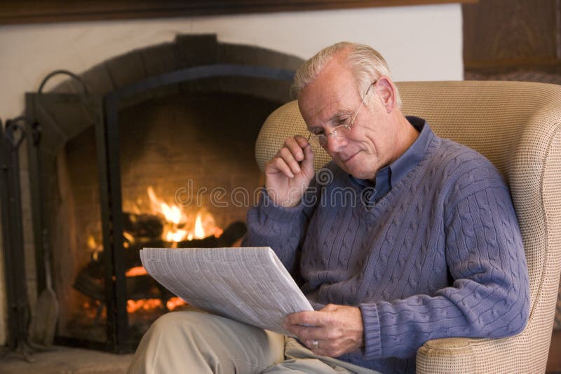 Man sitting in living room by fireplace with newspaper