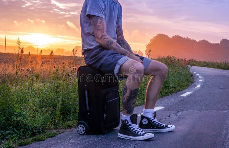 Man Sitting On Luggage On Road Side During Sunset Picture. Image: 109885676