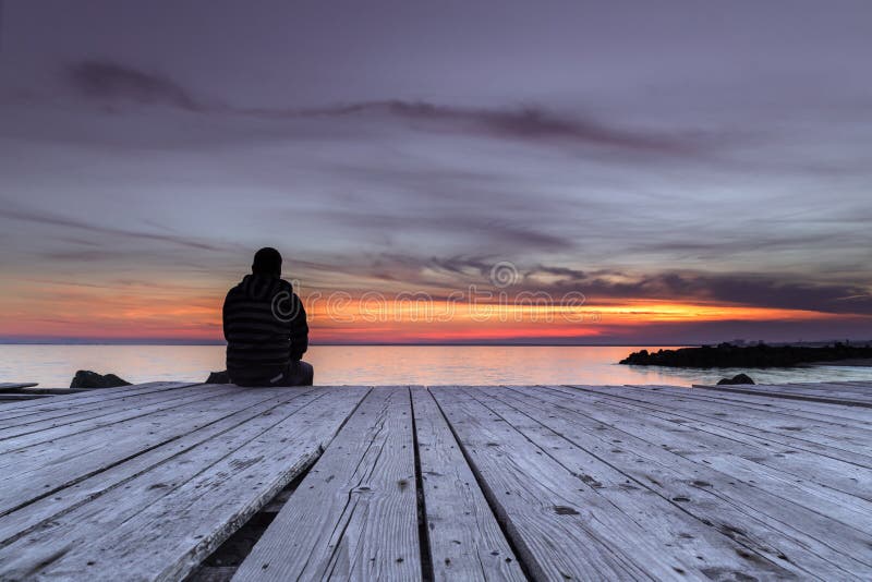 Man sitting on the pier and watching the sunset