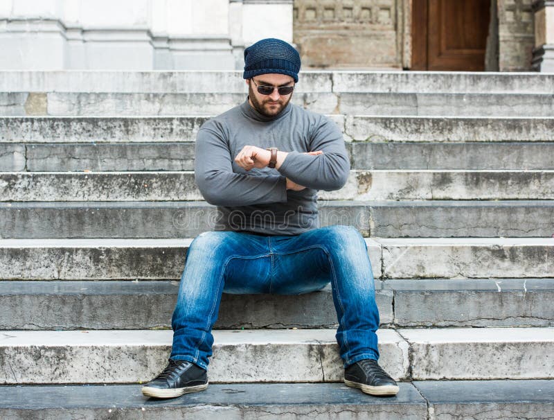 Man sitting on stairs and looking at his watch