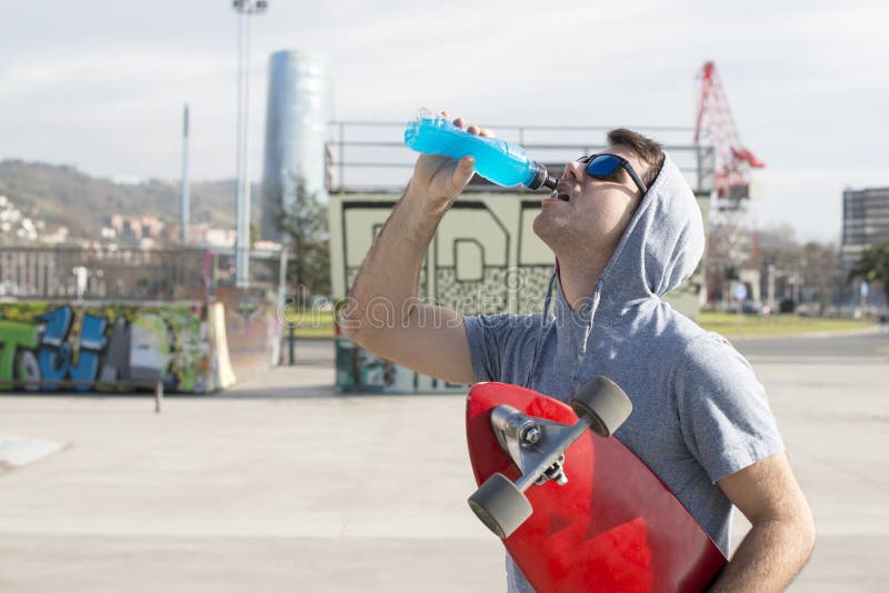 Man with skateboard drinking energy drink after sport.