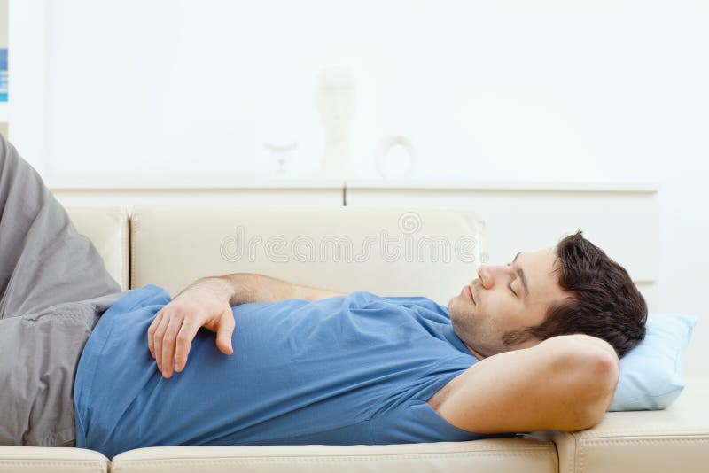 Young handsome man sleeping on couch at home, side view.