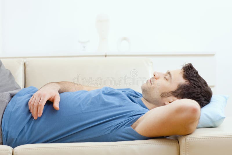 Young handsome man sleeping on couch at home, side view.