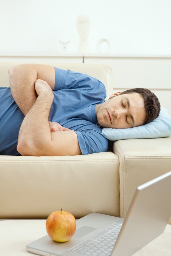 Young handsome man sleeping on couch at home, side view. Laptop computer on desk.