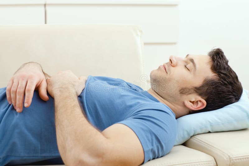 Young handsome man sleeping on couch at home, side view.