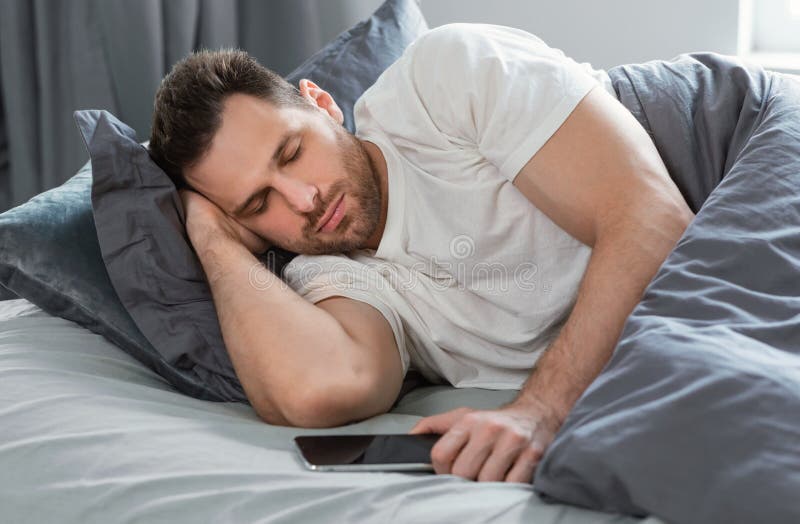Man Sleeping Holding Mobile Phone Lying in Bed at Home Stock Photo
