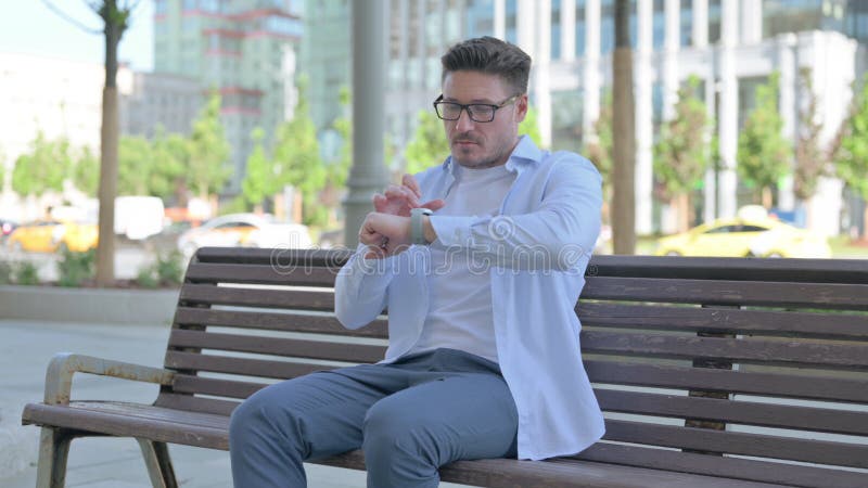 Man som använder smartch när man sitter utomhus på bänk royaltyfria foton