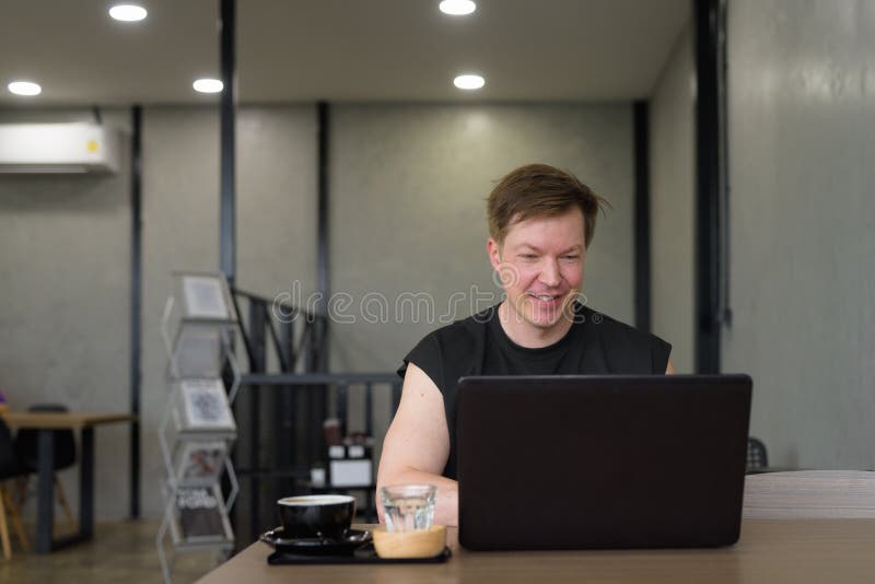 Man som arbetar med sin bärbara dator i ett café. Han ler och skriver med dator medan han ser glad ut. arkivbilder