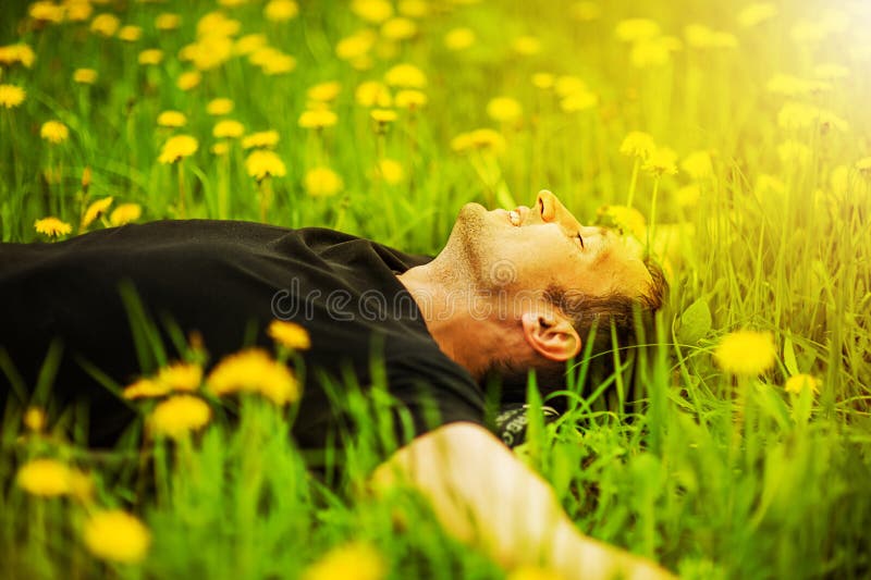 Happy smiling man lying on grass with yellow dandelion at sunny day. Happy smiling man lying on grass with yellow dandelion at sunny day