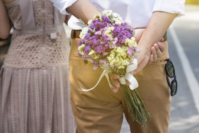 Man som rymmer blommabuketten som går bak kvinna ge sig för blommor arkivbilder Man som rymmer blommabuketten som går bak kvinna ge sig för blommor arkivbilder