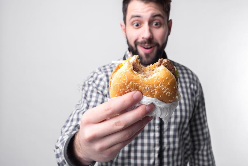 Man holding a piece of hamburger. student eats fast food. not helpful food. very hungry guy. Man holding a piece of hamburger. student eats fast food. not helpful food. very hungry guy.