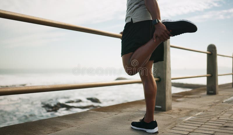 Man som springer och värmer upp ben vid strandsträckning och utomhusmiljö för att passa. sjöpromenad och manlig person arkivbild