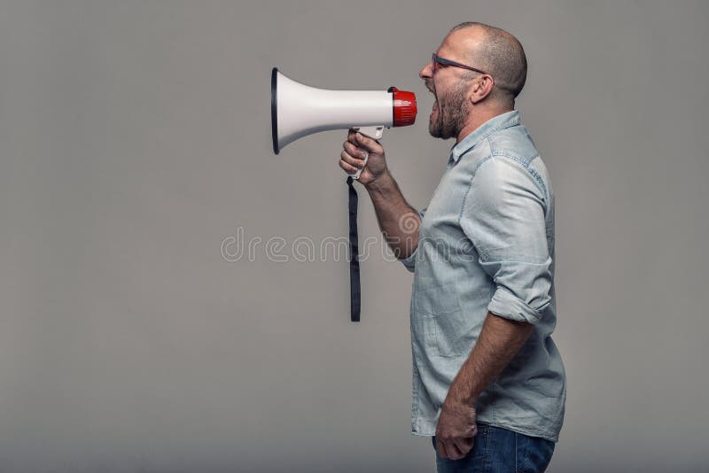 Man speaking over a megaphone as he makes a public address, participates in a protest or organises a rally or promotion, over grey with copy space to the side