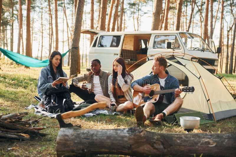 Man spelar gitarr. Ungdomsgruppen reser tillsammans i skogen på dagtid royaltyfri fotografi