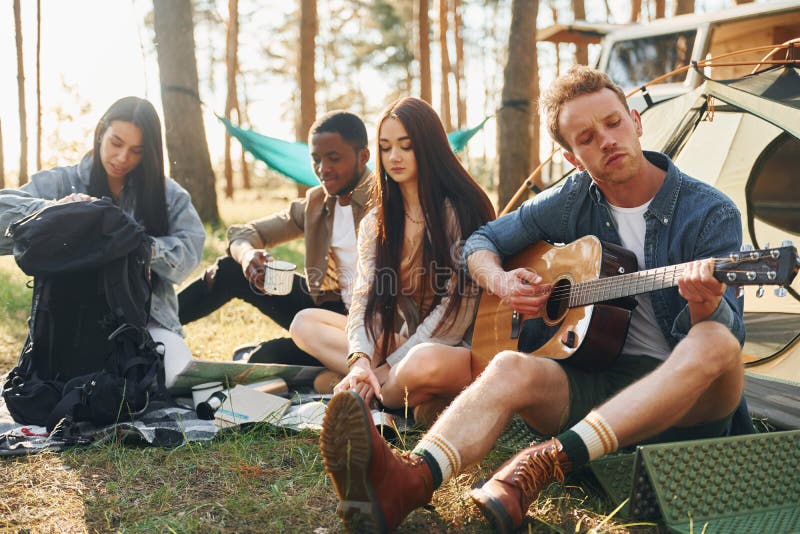 Man spelar gitarr. Ungdomsgruppen reser tillsammans i skogen på dagtid arkivfoto