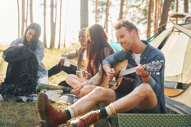 Man spelar gitarr. Ungdomsgruppen reser tillsammans i skogen på dagtid royaltyfri bild
