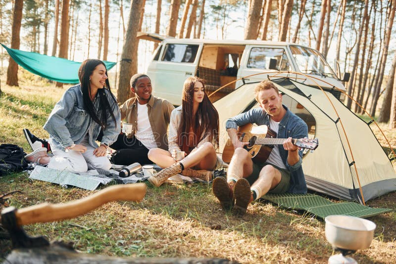 Man spelar gitarr. Ungdomsgruppen reser tillsammans i skogen på dagtid royaltyfria foton