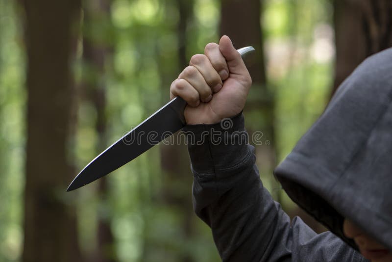 A man stabs with a large knife from above in the forest, close-up, selective focus. The concept: an attack on passers-by, a rapist